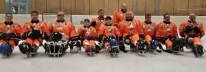 Squadra di hockey su ghiaccio in tuta arancione, seduta su slitte, con bastoni in mano.