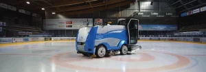Macchina spazzatrice blu e grigia su un campo di ghiaccio con pubblicità alle pareti.