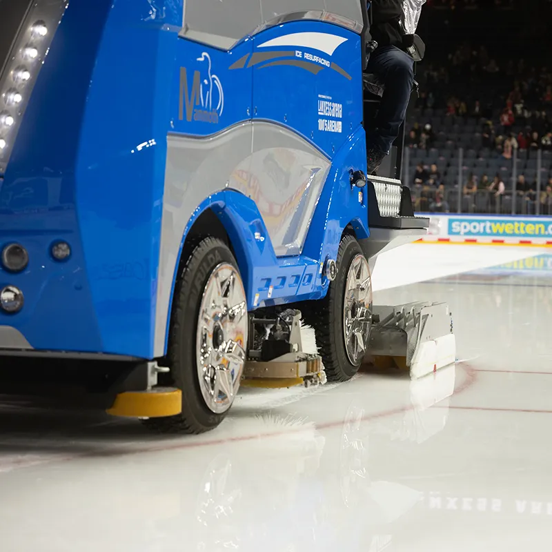 Blue vehicle for ice maintenance on the track, public in the stands.